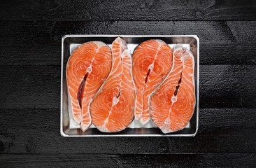 Salmon steaks on metal tray on black wooden table top view
