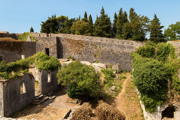 Fototapeta na wymiar Old ruined medieval fortress called Spagnola in Herceg Novi, Montenegro. Stone houses and walls covered by ivy and bushes. Historical place.
