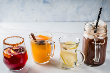 Selection of various autumn traditional drinks: hot chocolate with marshmallow, tea with lemon and ginger, white pumpkin spicy sangria, mulled wine. On white marble table, copy space, selective focus