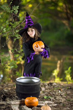 Litlle Halloween witch with pumpkin and kettle
