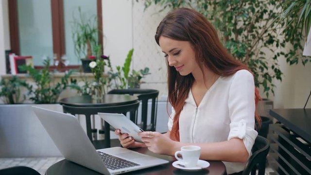 A beautiful girl sitting at the table in the pub and using her ipad. Medium shot. Soft focus.