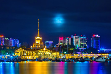 The building of the city seaport against the background of high-rise buildings at night, with the moonlight hidden behind the clouds. Mystical Sochi, Central Marine Station, Welcome to Russia 2018.