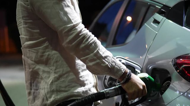 Young man fueling his car at gas station, using the pump nozzle. Late at night