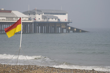 Lifeguard on duty flag on beach with Cromer pier and RNLI lifeboat station in the background