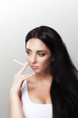 Obraz premium Smoke a young girl Beautiful young woman smoke a cigarette. Beautiful portrait. Girl with long black hair. The concept of health. On a gray background.