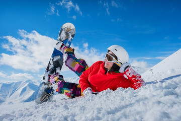Fototapeta na wymiar Beautiful girl snowboarder lies on the snow looking in the side.