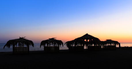 Silhouettes of hovels with the roofs covered with palm leaves for rest on the beach at sunset