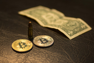 A close-up of a pistol cartridge with a bullet, a silver and gold bitcoin and one US dollar on a...