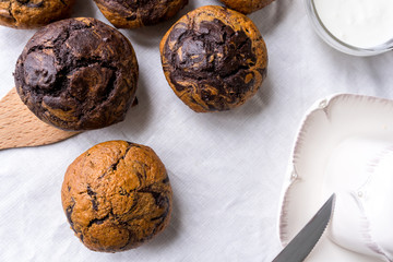 chocolate vanilla muffins on a linen tablecloth, beside an oil can and knife, top view