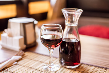 A decanter with red wine and a glass of red wine in a cafe on wooden table. Serving on the table.