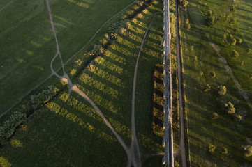 Aerial view of the ancient aqueduct of the Roman empire at sunset. The shadows of the arches of the aqueduct stand on a public green park.