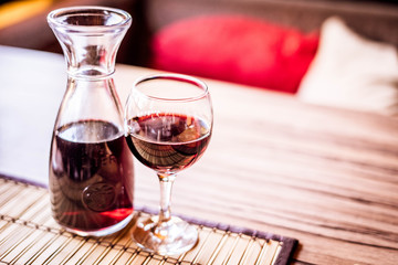 A decanter with red wine and a glass of red wine in a cafe on wooden table. Serving on the table.