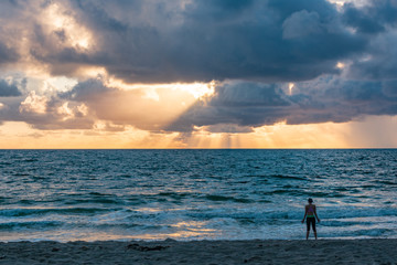Fototapeta na wymiar silhouette of female on a sandy beach enjoying the sun rising behind the clouds