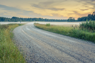  Sunset in countryside at mid summer. Hay rolls and road in misty weather with clear sunny sky. Beautiful nature in Latvia in August. 