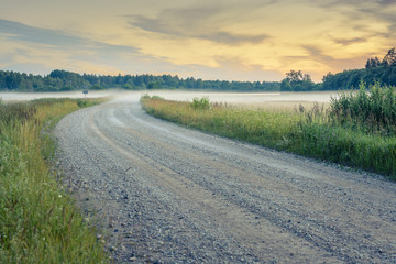  Sunset in countryside at mid summer. Hay rolls and road in misty weather with clear sunny sky. Beautiful nature in Latvia in August. 