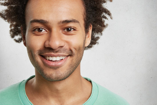 Close up portrait of bearded handsome man with bristle and curly bushy hair, smiles broadly, demonstrates white even teeth, isolated over white background. Happy teenager spends time with friends