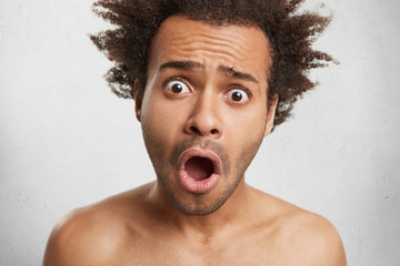 Puzzled surprised astonished mixed race male stares at camera with bugged eyes and opened mouth as...