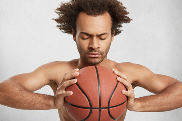 Indoor shot of serious concentrated basketball player with ball prepares alone for important match, uses all his knowledge, strength and skills for winning game. Professional sportsman with equipment