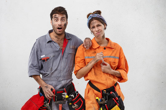 Two female and male maintenance workers being unwilling to repair kitchen tube, look with uspet and shocked expressions into camera, want to have holidays, pose against white blank copy space