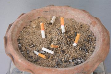 The rest of cigarettes in the ashtray. There are many types of cigarette stub on the sand in the ashtray.