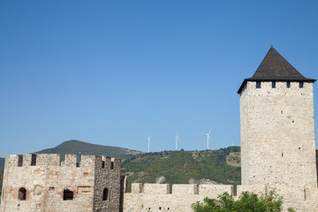 Fototapeta premium Romanian Wind Farm with Wind Turbine and windmills facing an old castle located on the Serbian side of the Danube river, in the Iron Gates valley.