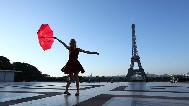 Slow motion of a happy cheerful girl dancing near Eiffel Tower with a red umbrella, Paris, France