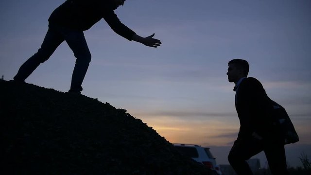 Businessman silhouette gived hand for pull team to peak mountain work together