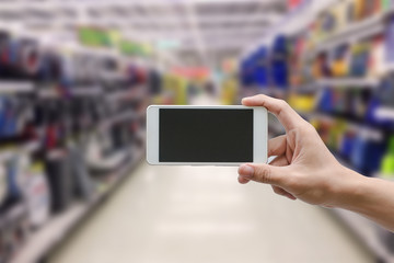 hand holding mobile smart phone with blank monitor screen on Supermarket blur background, business concept