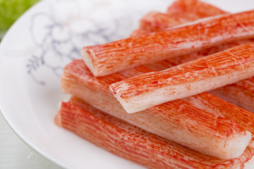 Red crab stick in a white plate. And green lettuce and coriander, pepper and other spices. 