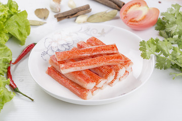 Red crab stick in a white plate. And green lettuce and coriander, pepper and other spices. 