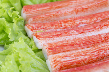 Red crab stick in a white plate. And green lettuce and coriander, pepper and other spices. 