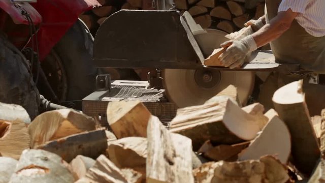 Male workers cutting firewood logs with circular saw powered by tractor engine - sliding camera