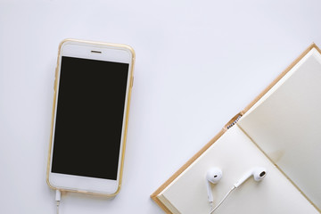 Smartphone with earphone and notebook on white table background