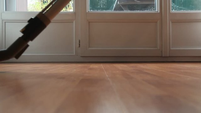 Vacuum cleaner being passed on wooden floor of modern apartment