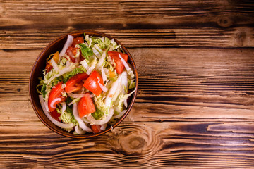 Dietary salad with the chinese cabbage and tomatoes in ceramic bowl on a wooden table. Top view