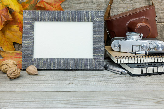 classic camera, notebooks, fountain pen, empty photo frame on wooden background with dried vibrant leaves