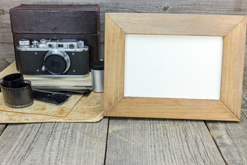 vintage camera, negative films, old photos and empty frame on grunge wooden table