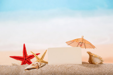 Fototapeta na wymiar A blank card, starfish, umbrella and sea shells in the sand against the background of sea.
