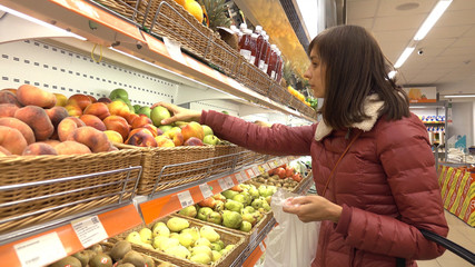 Woman in supermarket selects fruit and vegetables.
