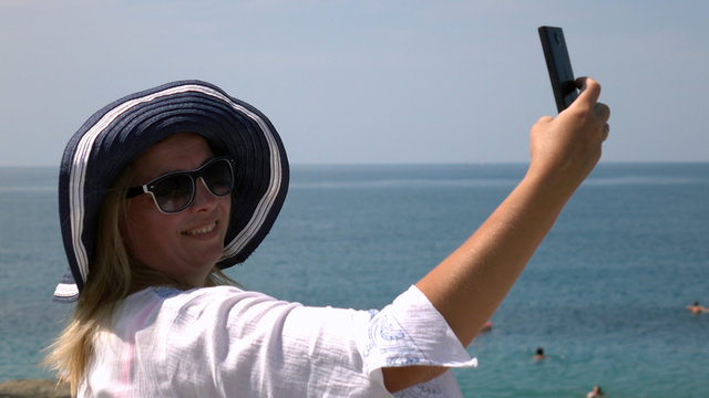 Happy woman in hat , making a selfie on the beach taking photographs with a smartphone.