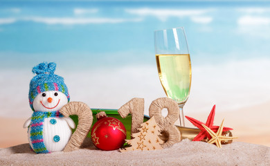 New Year inscription 2018, ball instead number 0, bottle and glass champagne, snowman, Christmas tree, starfish in sand.