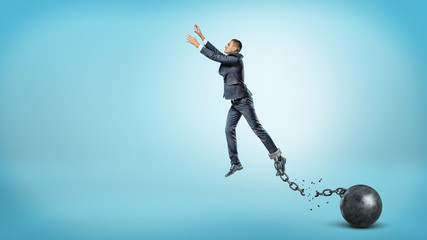 A businessman leaps up with outstretched hands while he's chained to an iron ball with a broken...