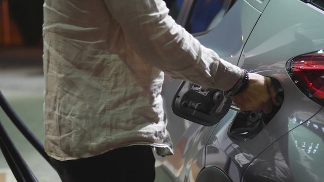 Young Man Fueling His Car At Gas Station, Using The Pump Nozzle. Late At Night