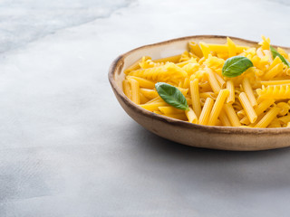 Italian raw short pasta in a dish with basil leaves on gray background