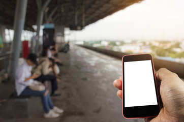 hand using mobile phone with blank screen over blurred view of people waiting sky train at train station, internet, social media technology and network connection concept