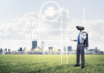 Camera headed man standing on green grass against modern citysca