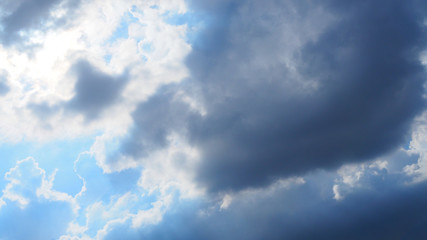 Dark black big chunk grey cloudy sky, with bright sunlight shining out through, from light blue sky background