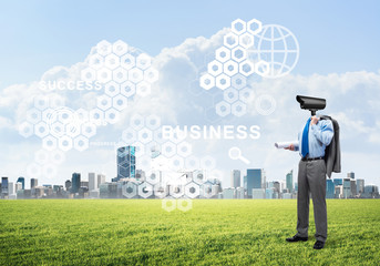 Camera headed man standing on green grass against modern cityscape