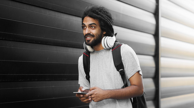 Casual young hipster with dreadlocks listening music holding mobile phone.