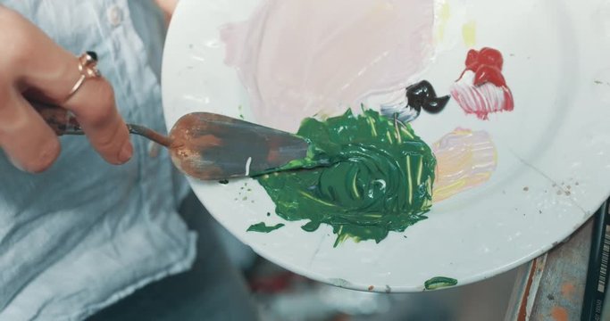 Close up video of mixing acrilic paint on a palette, painting in a studio